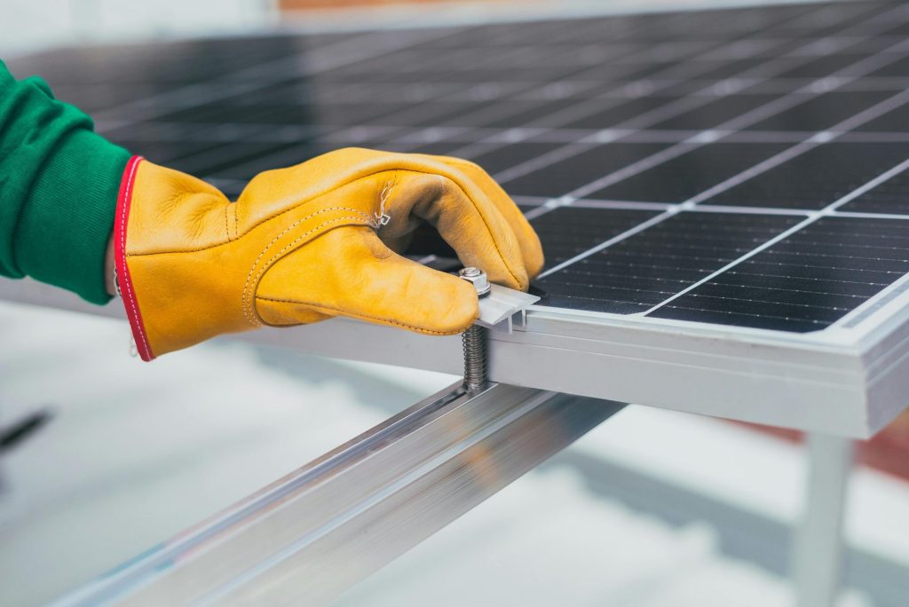 Nahaufnahme der Hand eines Arbeiters mit Schutzhandschuhen, der eine Schraube an einem Solarpanel einstellt.